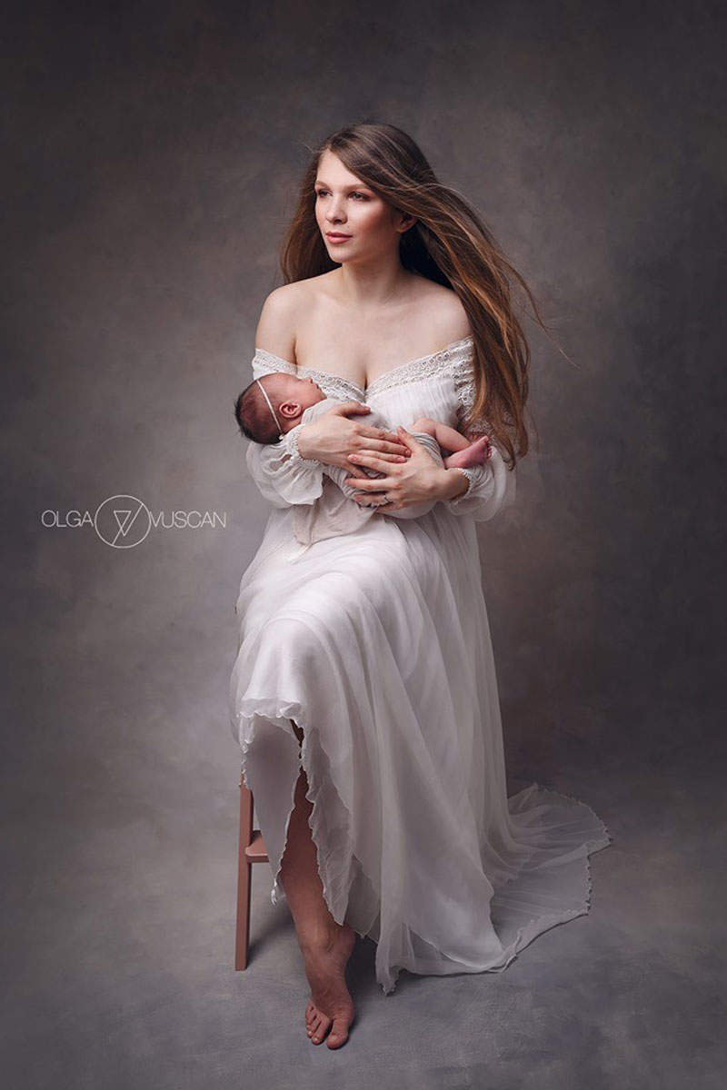 Olga Vuscan New Born Photographer for Workshops by Camen Bergmann Studio mother in luxurious white dress sits on a stool and holds her new born baby